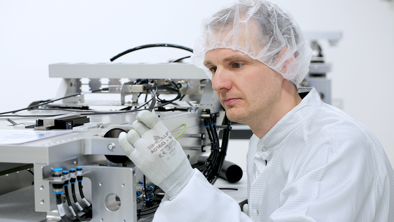 Technicians in cleanroom assembling precision drive components at a workstation