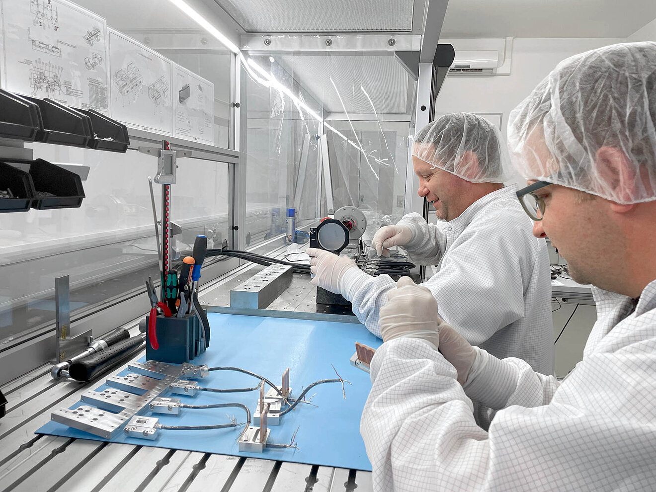 Technicians in cleanroom assembling precision drive components at a workstation